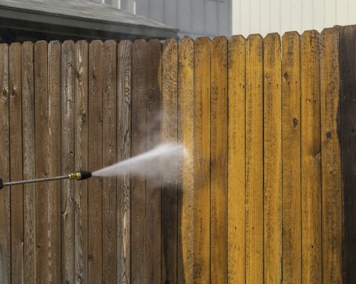 Living in a home maintenance Spraying the top of a Wooden fence spraying a high Pressure washing a dirty grimy old wooden fence and turning it from dirty to clean in a matter of second with spray blast from pressure washer with grass and sidewalk